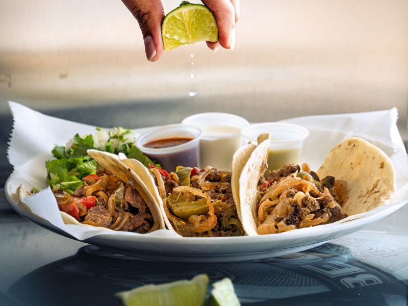 a plate of tacos with a lime being drizzled on top